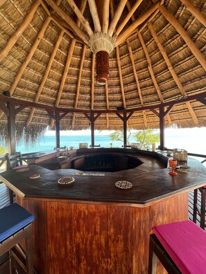 Een houten bar met rieten dak, met uitzicht op een strand.