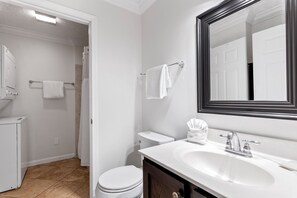 Une salle de bain avec des toilettes blanches, un lavabo avec un miroir et un espace douche.