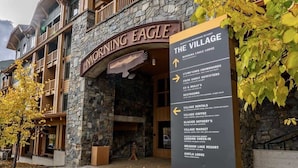 A stone building with a sign for 'Morning Eagle Lodge' and a directional sign for 'The Village' with amenities listed. - Ski In / Ski Out Condo, Amazing Views, Sleeps 8! (Whitefish)