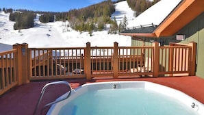 A hot tub with a view of a snowy mountain slope and a wooden fence. - Ski In / Ski Out Condo, Amazing Views, Sleeps 8! (Whitefish)