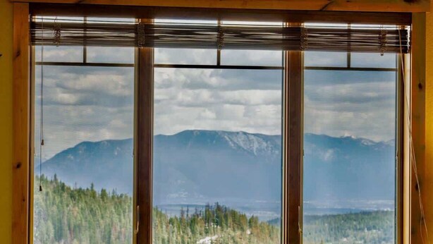 A room with a large window offering a view of a forest and mountains. - Ski In / Ski Out Condo, Amazing Views, Sleeps 8! (Whitefish)