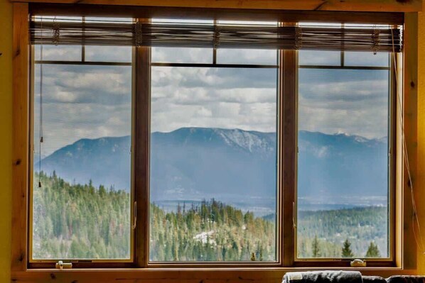 A room with a large window offering a view of a forest and mountains.