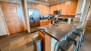 A modern kitchen with wooden cabinets, stainless steel appliances, and a granite countertop. - Ski In / Ski Out Condo, Amazing Views, Sleeps 8! (Whitefish)