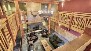 A spacious room with a fireplace, leather armchairs, a chandelier, and wooden paneling. - Ski In / Ski Out Condo, Amazing Views, Sleeps 8! (Whitefish)