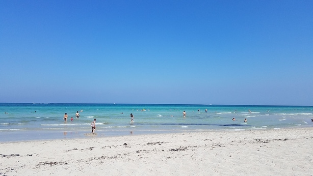 A beach with clear blue water and a sandy shore.