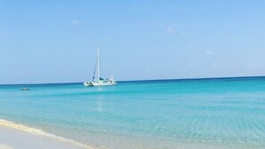 A beach with clear turquoise water and a sailboat in the distance. - “Our Paradise Found” Condo 1405 at Infinity Bay (West Bay Beach, Roatan)