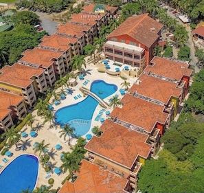 Ein Resort mit mehreren Gebäuden, einem zentralen Schwimmbad und umliegenden Palmen.