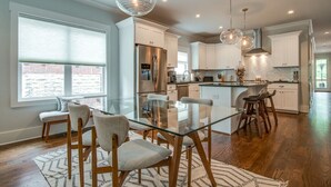 A modern kitchen with a glass dining table, white cabinets, and stainless steel appliances.