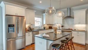 A modern kitchen with white cabinetry, stainless steel appliances, and a central island with bar stools.