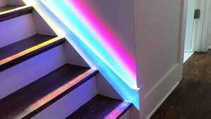 A staircase with wooden steps and a colorful LED light strip along the edge.