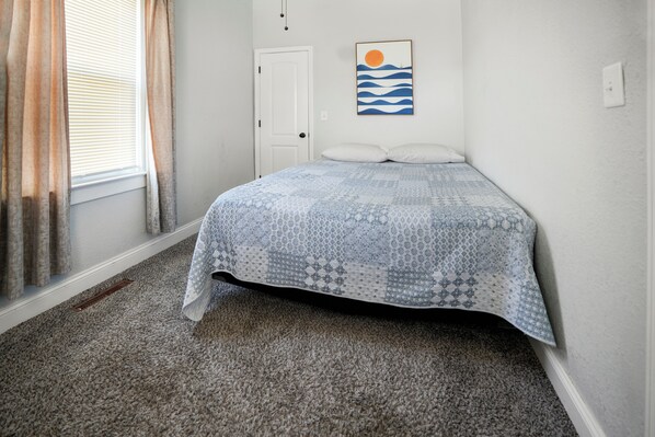 Un dormitorio con cama, una puerta, una ventana con cortinas y una obra de arte colgada en la pared.