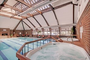 An indoor swimming pool with a hot tub, wooden deck, and brick walls.