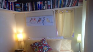 Ein ordentlich bezogenes Bett mit einem Blumenkissen, zwei Nachttischlampen und einem Bücherregal voller Bücher.
