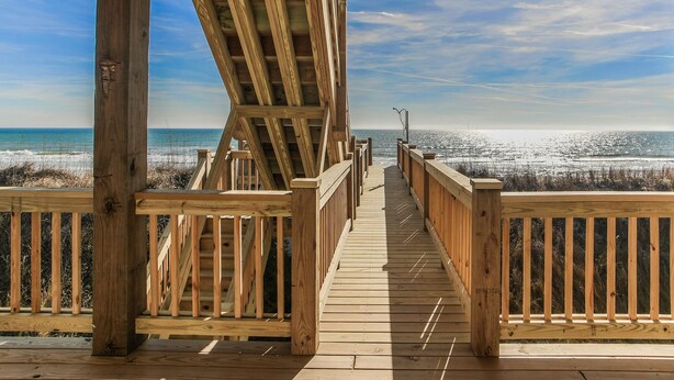 Eine Holzterrasse führt zu einem Strand mit freiem Blick auf das Meer.
