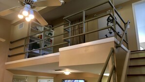 Un espacio habitable de varios niveles con una escalera, un ventilador de techo, un televisor y una estantería.