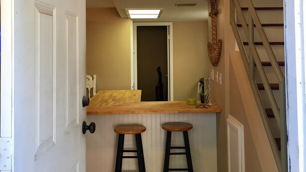 Un interior de varios niveles con una escalera, una barra de madera con taburetes y una puerta con un ventanal decorativo.