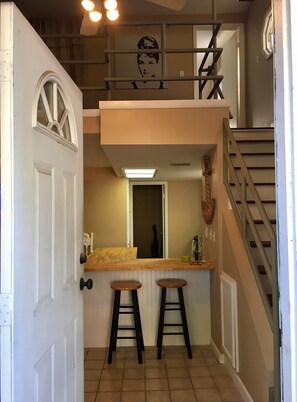 Un intérieur à plusieurs niveaux, avec un escalier, un comptoir en bois doté de tabourets et une porte ornée d’un vitrail décoratif.