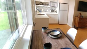 Een moderne keuken met witte kasten, een magnetron en een koelkast. Er staat een eettafel met borden en bekers.