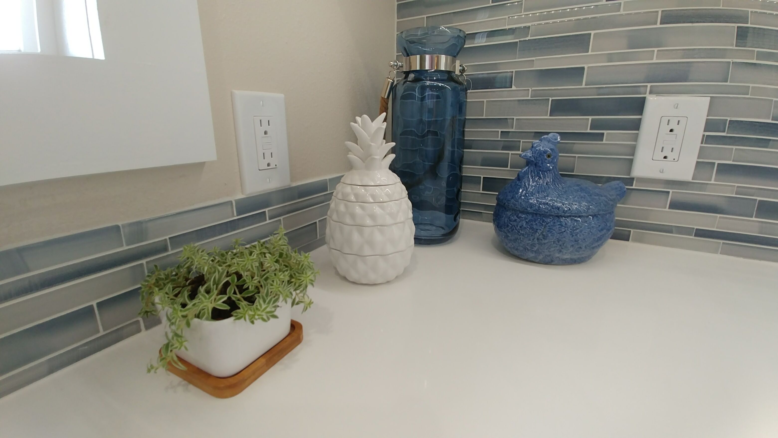 A kitchen counter with a potted plant, a pineapple-shaped container, and a blue ceramic pot.