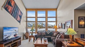 A cozy living room with a large window, a television, a sofa, a coffee table, and various decorative items. - RMR: Greyling 4513 Condo in The Aspens/Wilson,WY (Wilson)