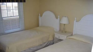 Un dormitorio con dos camas individuales, una mesita de noche con lámpara y una ventana con persianas.