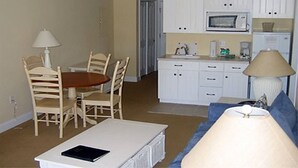 Cocina compacta con armarios blancos, microondas y cafetera. Hay una mesa de comedor con sillas y una lámpara.