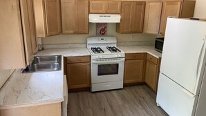 A compact kitchen with wooden cabinets, a white stove, a sink, and a refrigerator.
