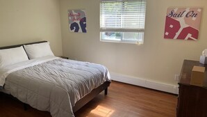 A bedroom with a bed, a window with blinds, and two wall art pieces.