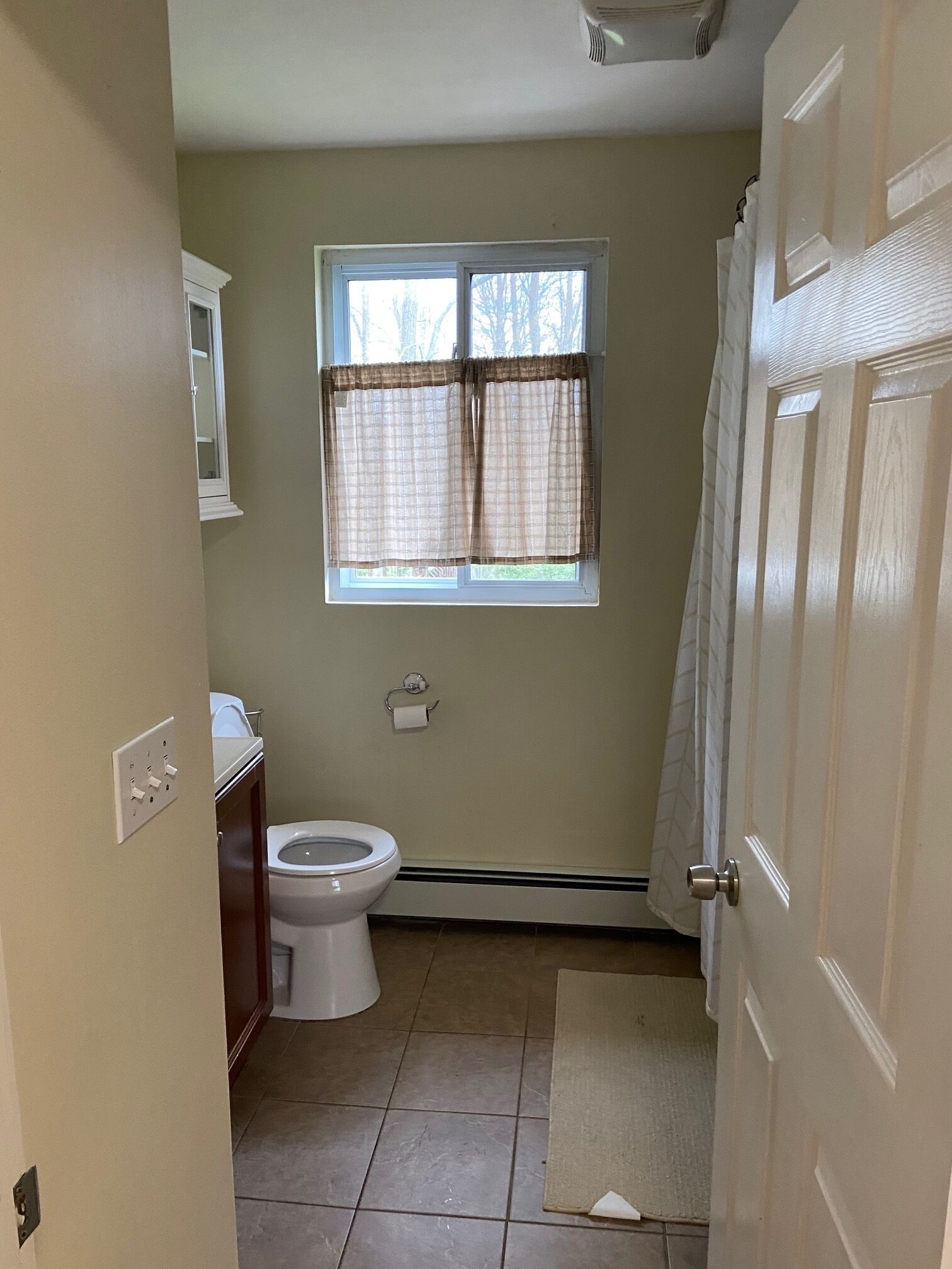 A small bathroom with a toilet, a window with curtains, a towel rack, and a door.