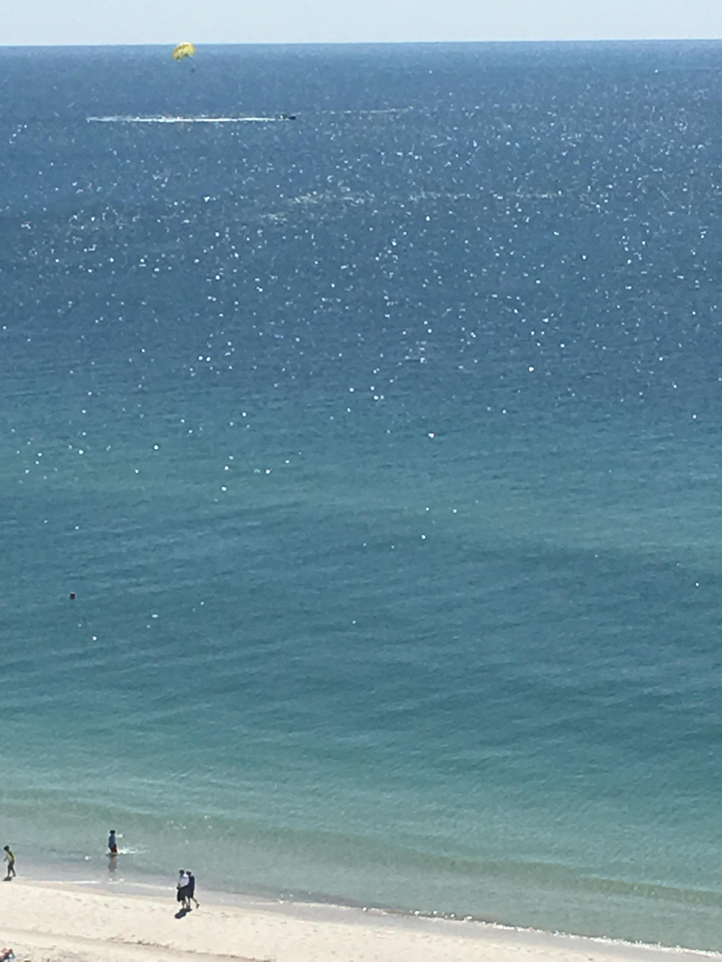Een strand met helderblauw water en enkele mensen die langs de kust lopen.
