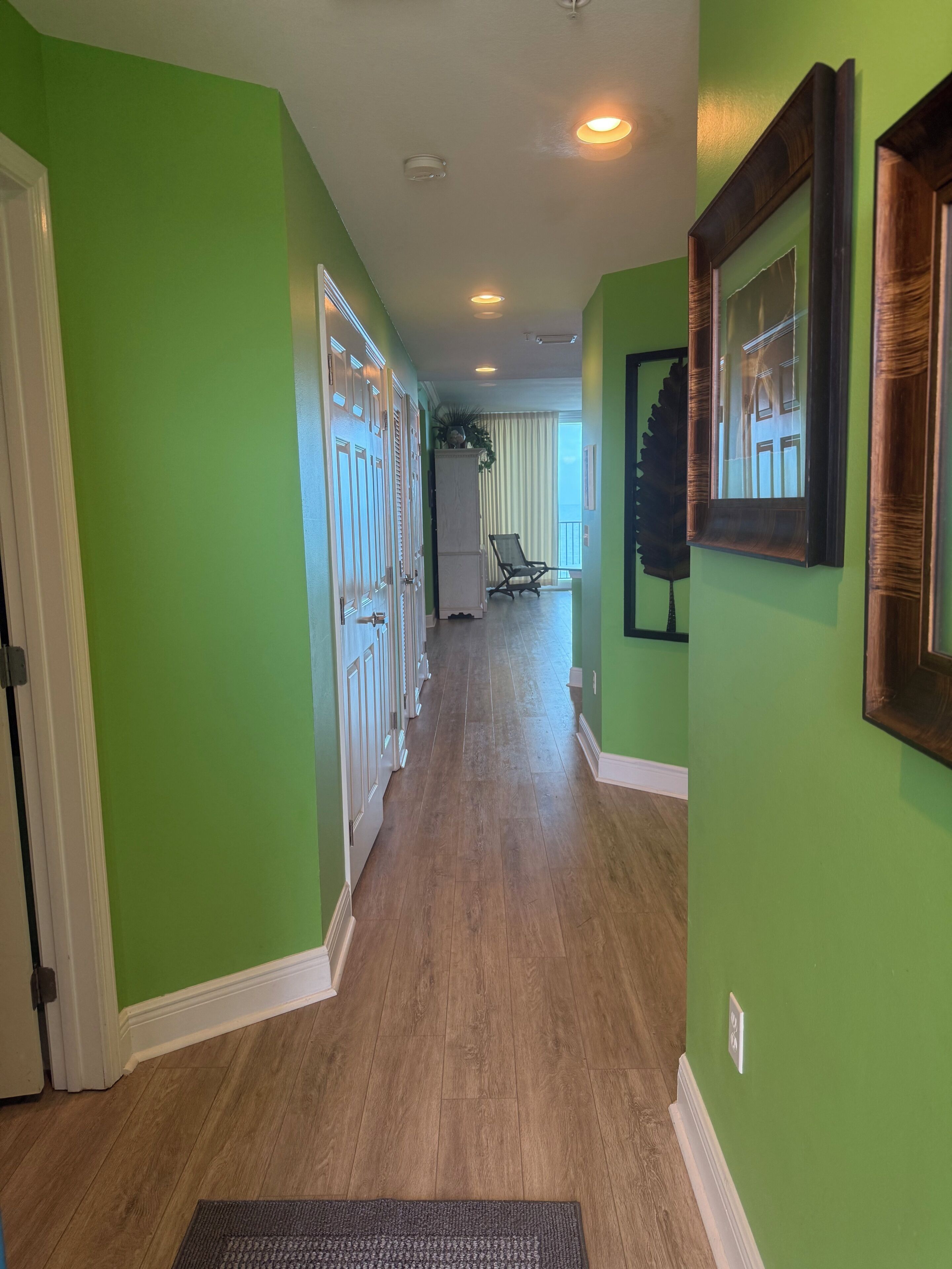 A hallway with green walls, wooden flooring, and a door at the end.