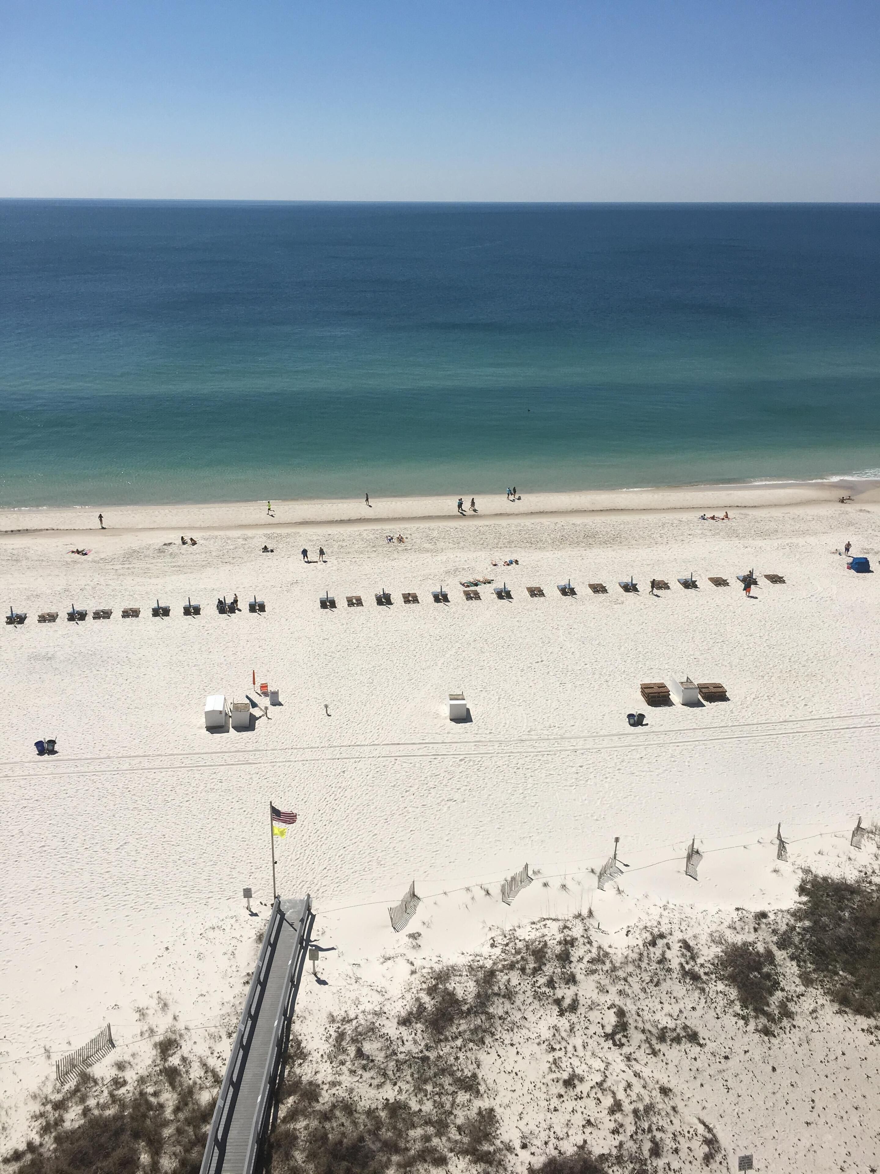 A beach with rows of sun loungers and a flagpole with flags.