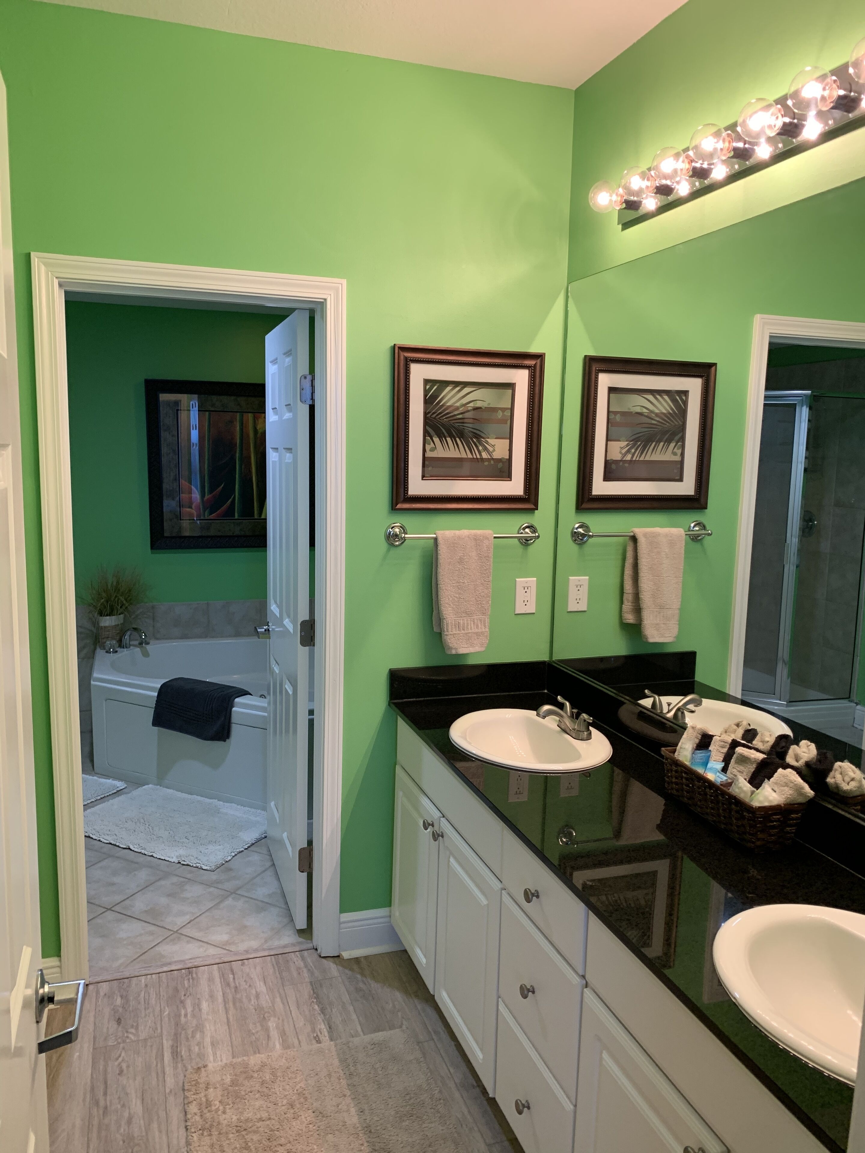 Un baño con paredes verdes, dos lavamanos, una bañera y un tocador con espejo.
