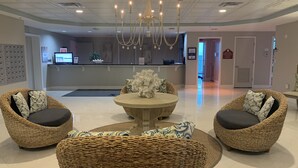 A lobby with wicker furniture, a central round table, and a reception desk in the background.