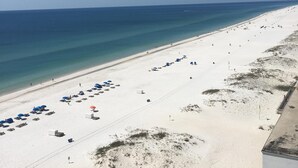 A beach with white sand, clear blue water, and a few umbrellas.