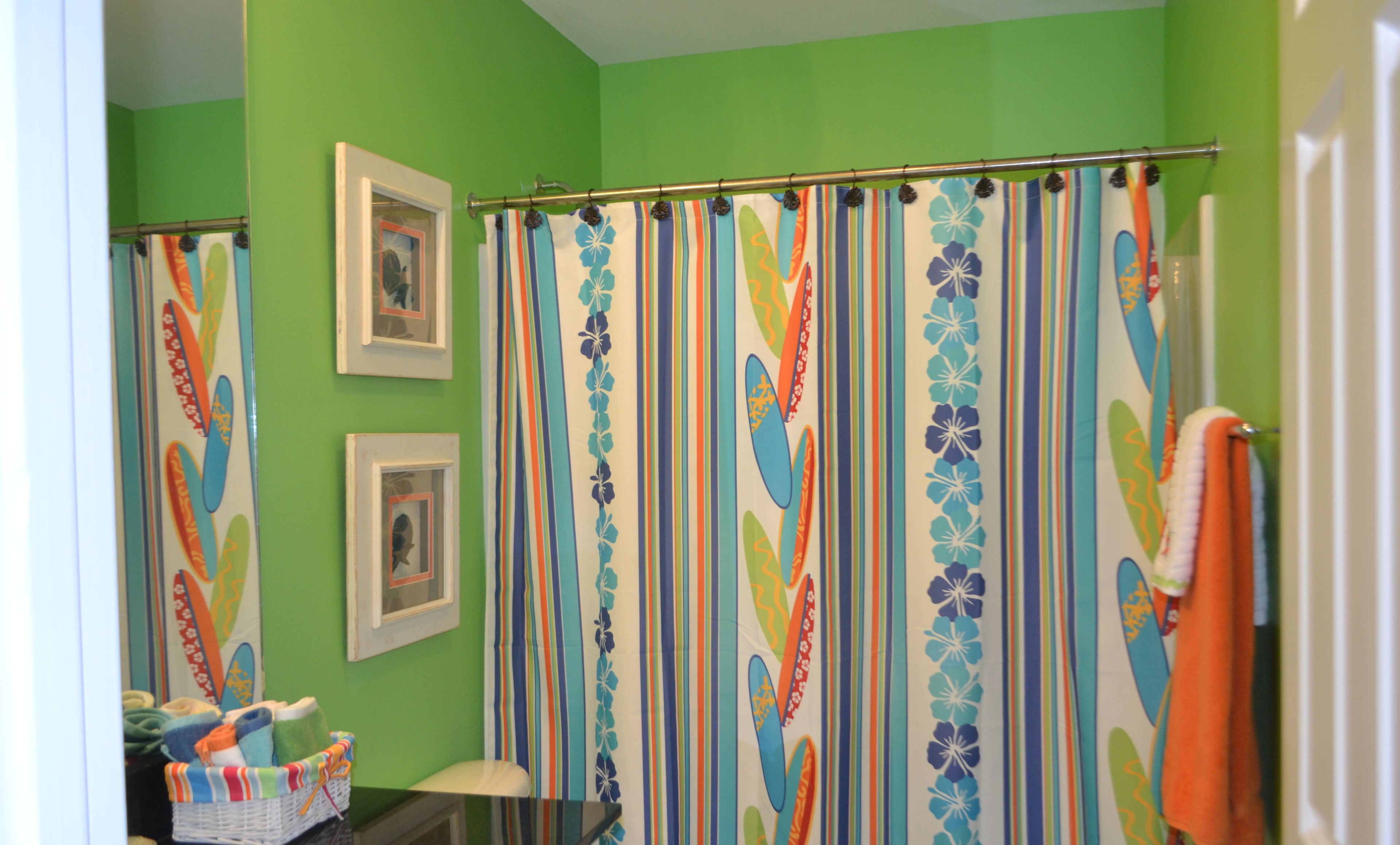 Un baño con paredes verdes, una cortina de ducha estampada con motivos florales, un lavabo y un perchero para toallas.