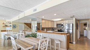 A modern kitchen with white cabinets, a stainless steel refrigerator, and a wooden island with stools. - BREATHTAKING VIEWS on every floor! 214 Destin Seafarer (Destin)