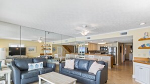 A spacious living room with two grey leather sofas, a coffee table, and a TV. A kitchen is visible in the background with white cabinets and stainless steel appliances. - BREATHTAKING VIEWS on every floor! 214 Destin Seafarer (Destin)