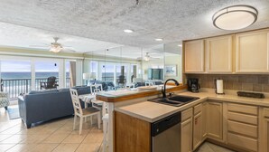 A spacious living area with a large sofa, dining table, and chairs. There is a kitchen with a sink, stove, and cabinets. The room has large windows offering a view of the ocean. - BREATHTAKING VIEWS on every floor! 214 Destin Seafarer (Destin)