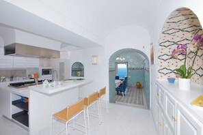 A modern kitchen with white cabinetry, a central island with bar stools, and a patterned tile backsplash.