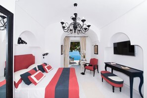 A hotel room with a bed, a desk, a chair, a TV, and a view of the sea.