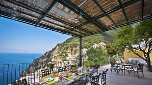 A terrace with a table set for dining, overlooking a coastal landscape with buildings on a hillside. - The Most Panoramic Villa In The Center Of Positano (Positano)