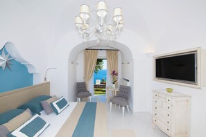 A modern bedroom with a bed, two armchairs, a dresser, a TV, and a view through an arched doorway.