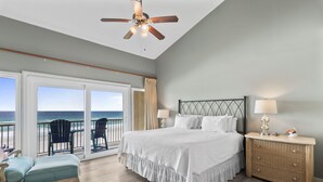 Camera da letto con un letto grande, un comodino, una consolle in vimini, una ventola a soffitto e vista sull'oceano tramite una porta scorrevole in vetro.