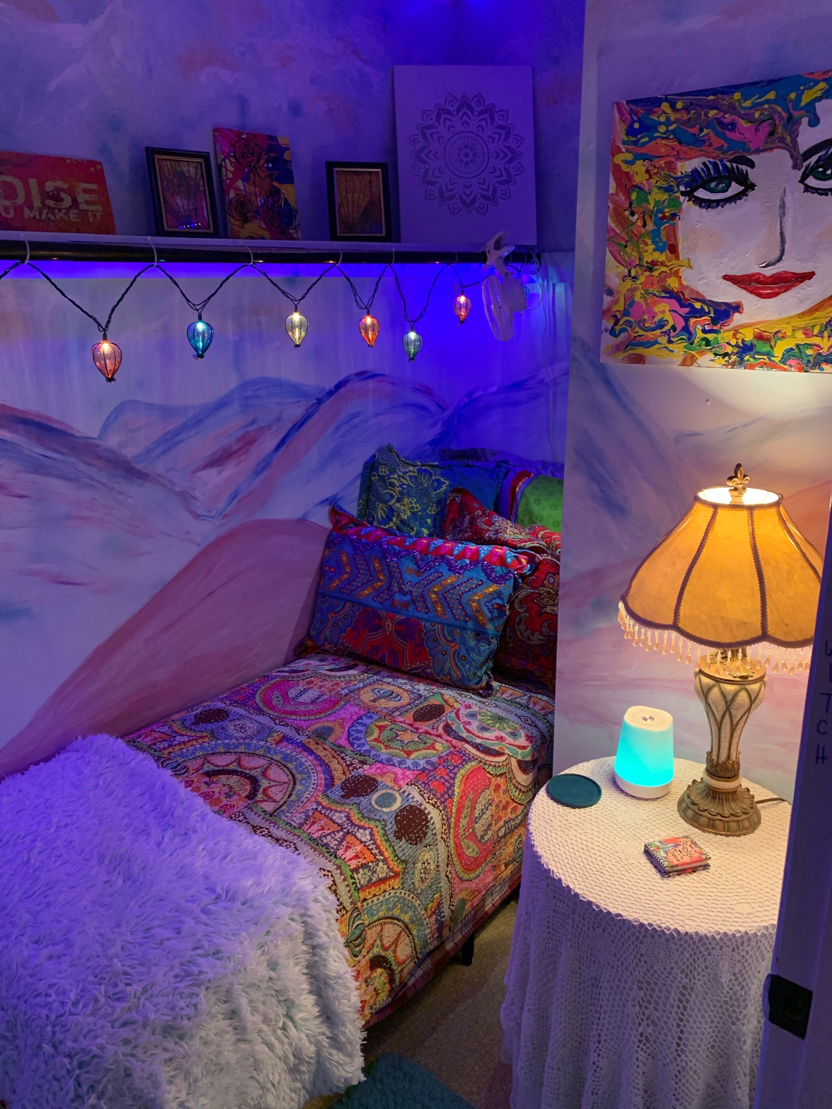A cozy bedroom with a colorful bedspread, a fluffy white rug, a bedside lamp, and string lights.