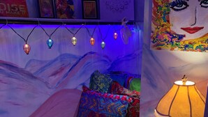 Un dormitorio acogedor con una colcha de colores, una alfombra blanca mullida, una lámpara de noche y luces de cadena.
