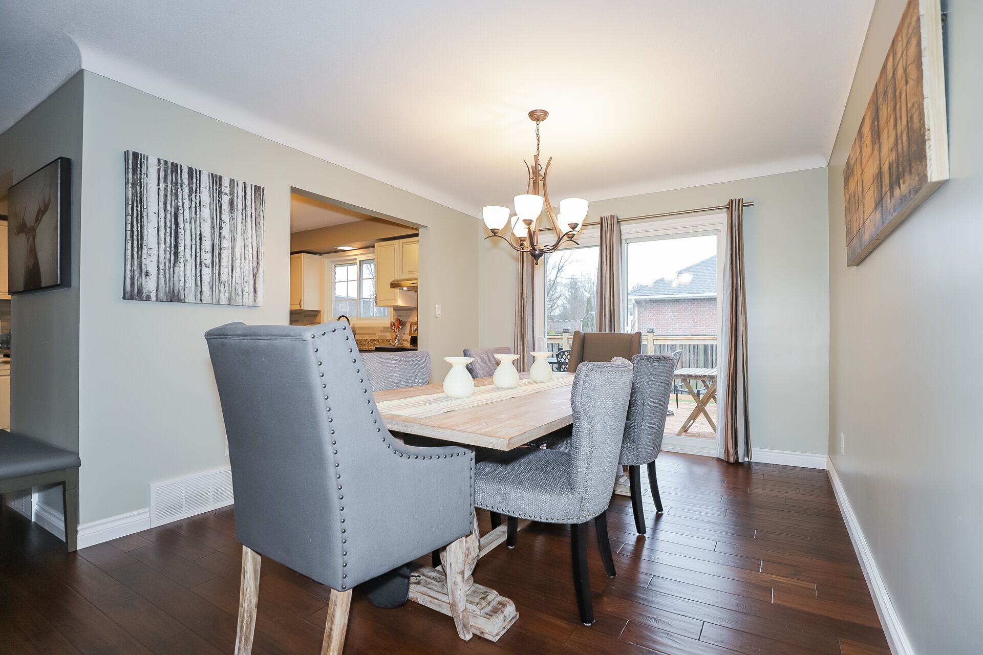 A dining area with a wooden table, grey upholstered chairs, and a chandelier.