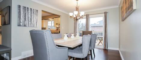 A dining area with a wooden table, grey upholstered chairs, and a chandelier.