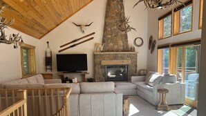 Una sala de estar acogedora con una chimenea de piedra, un televisor de pantalla plana grande y un techo de madera.