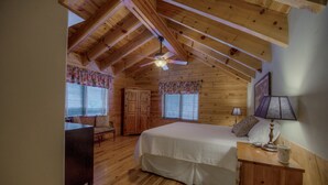 Un dormitorio con techo de madera, una cama, una mesita de noche, una lámpara y una ventana con persianas.
